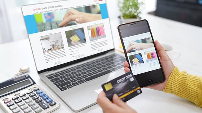 Nesten alle nettaktiviteter kan bidra til det digitale fotavtrykket ditt. Bildet viser noen som holder telefonen og kredittkortet sitt foran en dataskjerm med et shoppingvindu på nettet åpent.
